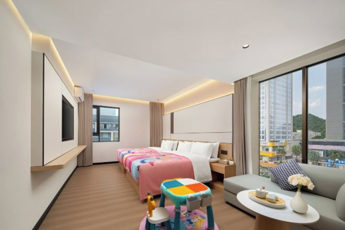 Une chambre d’hôtel avec un lit, un canapé, une télévision et une grande fenêtre.