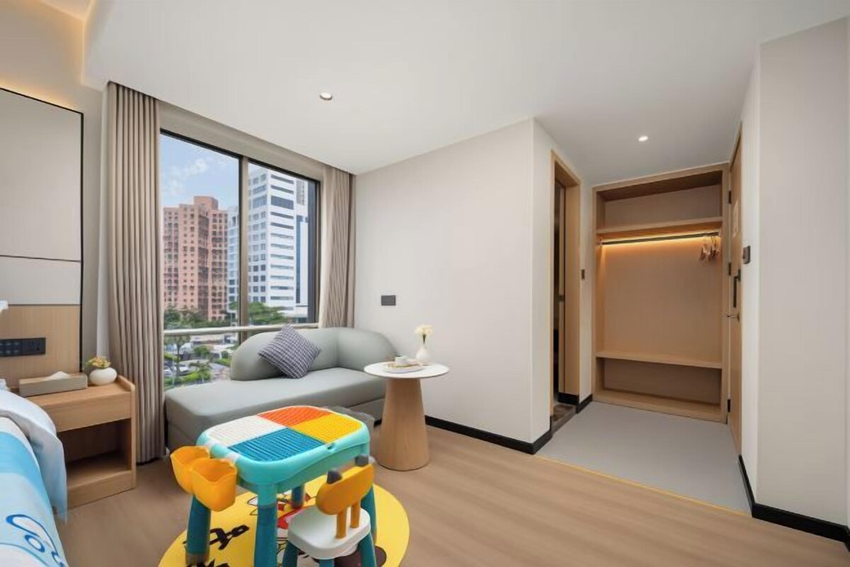 Habitación de hotel con cama, una mesita, sofá, zona de juegos y vistas a la ciudad.