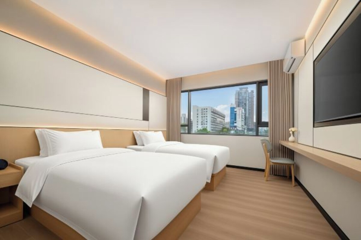 Une chambre d’hôtel avec deux lits, un bureau, une chaise et une grande fenêtre donnant sur la ville.