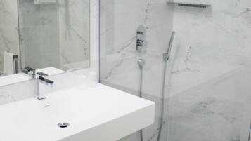Un baño moderno con lavamanos de mármol blanco, ducha con cerramiento de vidrio y un espejo grande.
