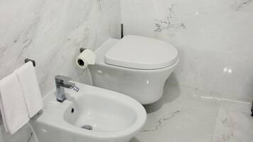 A bathroom with a bidet, toilet, and marble walls.