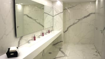 A modern bathroom with a marble floor and wall, a large mirror, and a white vanity with three sinks.