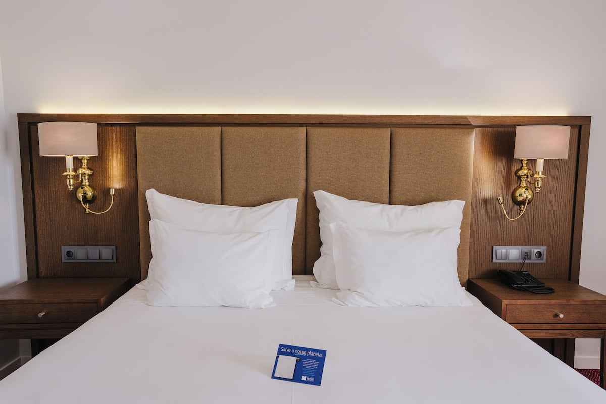 A hotel room with a large bed, two bedside tables, a nightstand, a lamp, and a sign on the bed.