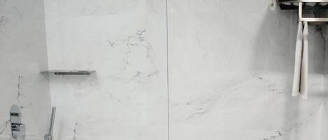 Un baño moderno con cabina de ducha de vidrio, paredes de mármol y lavamanos blanco.