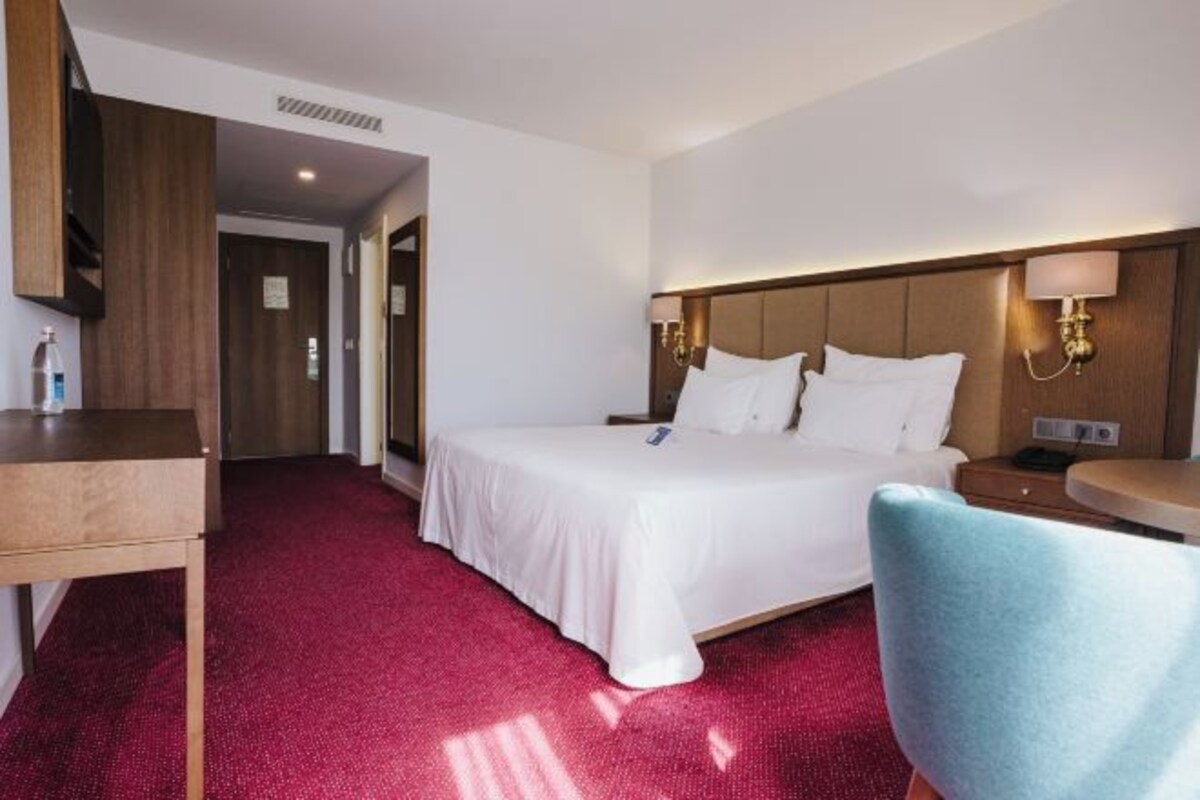 A hotel room with a bed, a desk, a chair, and a nightstand.