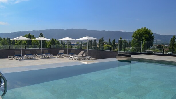A swimming pool with lounge chairs and umbrellas, surrounded by a fence, with a mountain view in the background.
