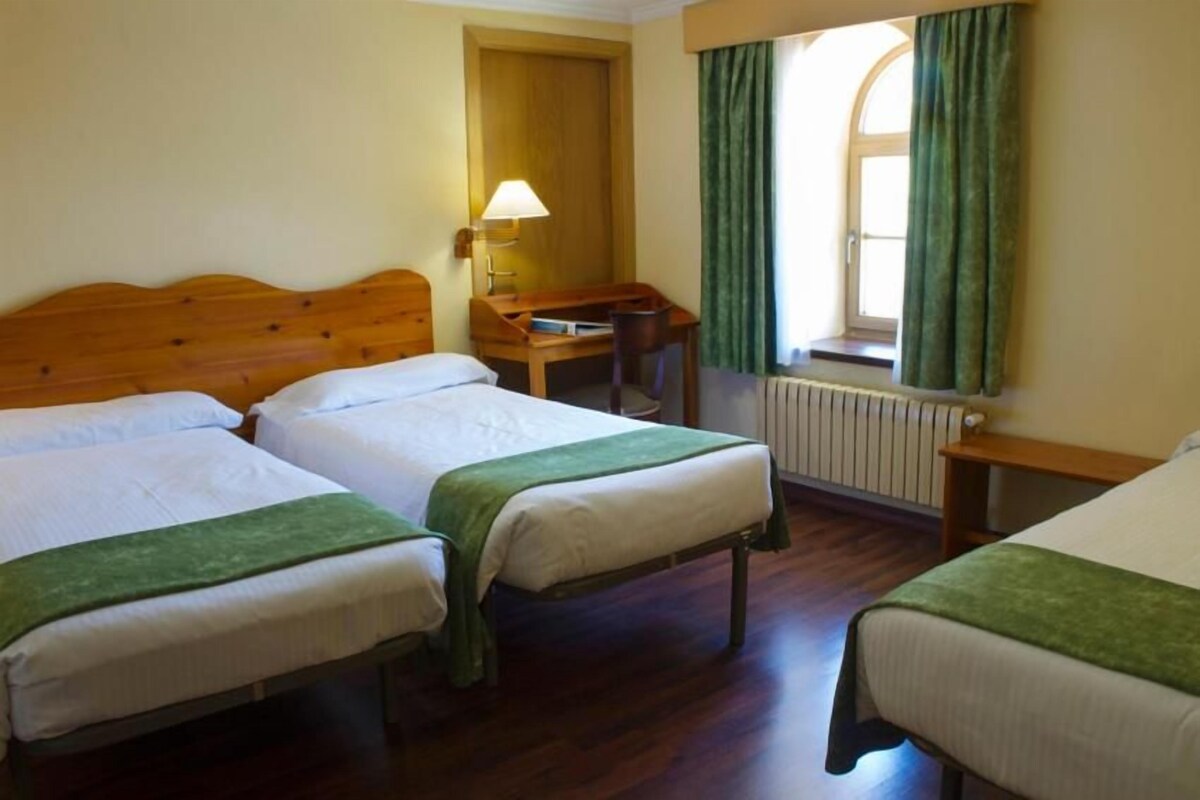 A hotel room with two beds, a desk, a lamp, and a window with curtains.
