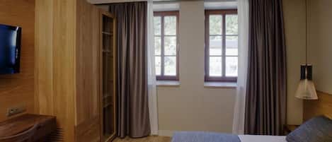 Une chambre d’hôtel avec un lit, une télévision, une armoire en bois, une fenêtre avec des rideaux et une lampe.