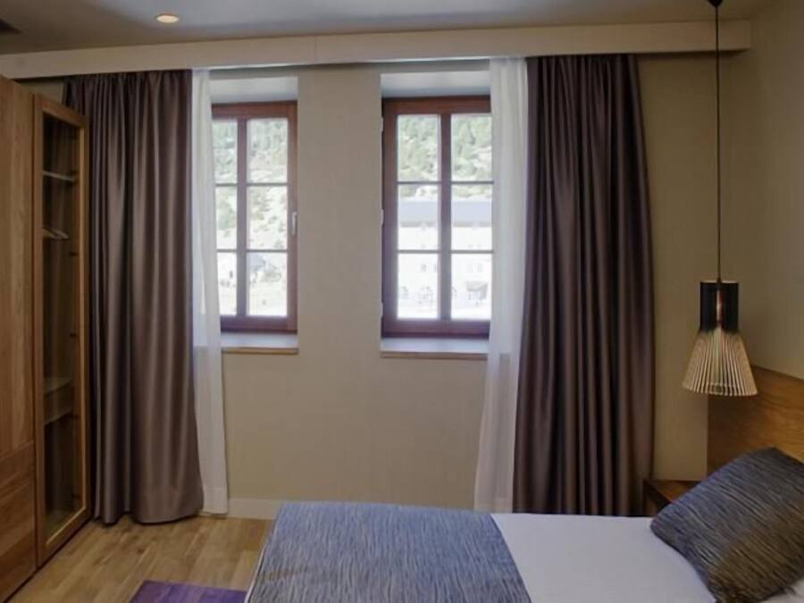 Habitación de hotel con una cama, televisión, armario de madera, ventana con cortinas y una lámpara.