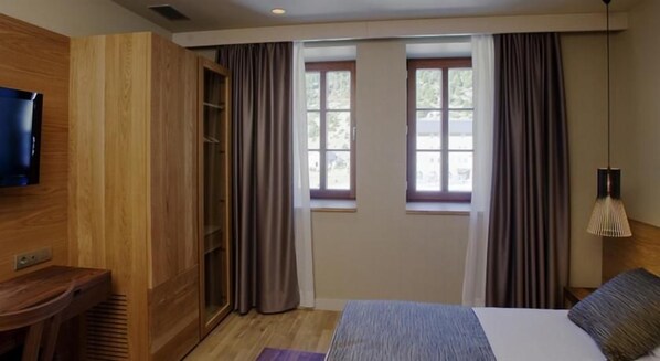 A hotel room with a bed, a TV, a wooden wardrobe, a window with curtains, and a lamp. - Vall de Nuria (Queralbs)
