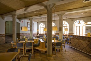 A restaurant with wooden tables and chairs, large windows with arched tops, and hanging pendant lights. - Vall de Nuria (Queralbs)