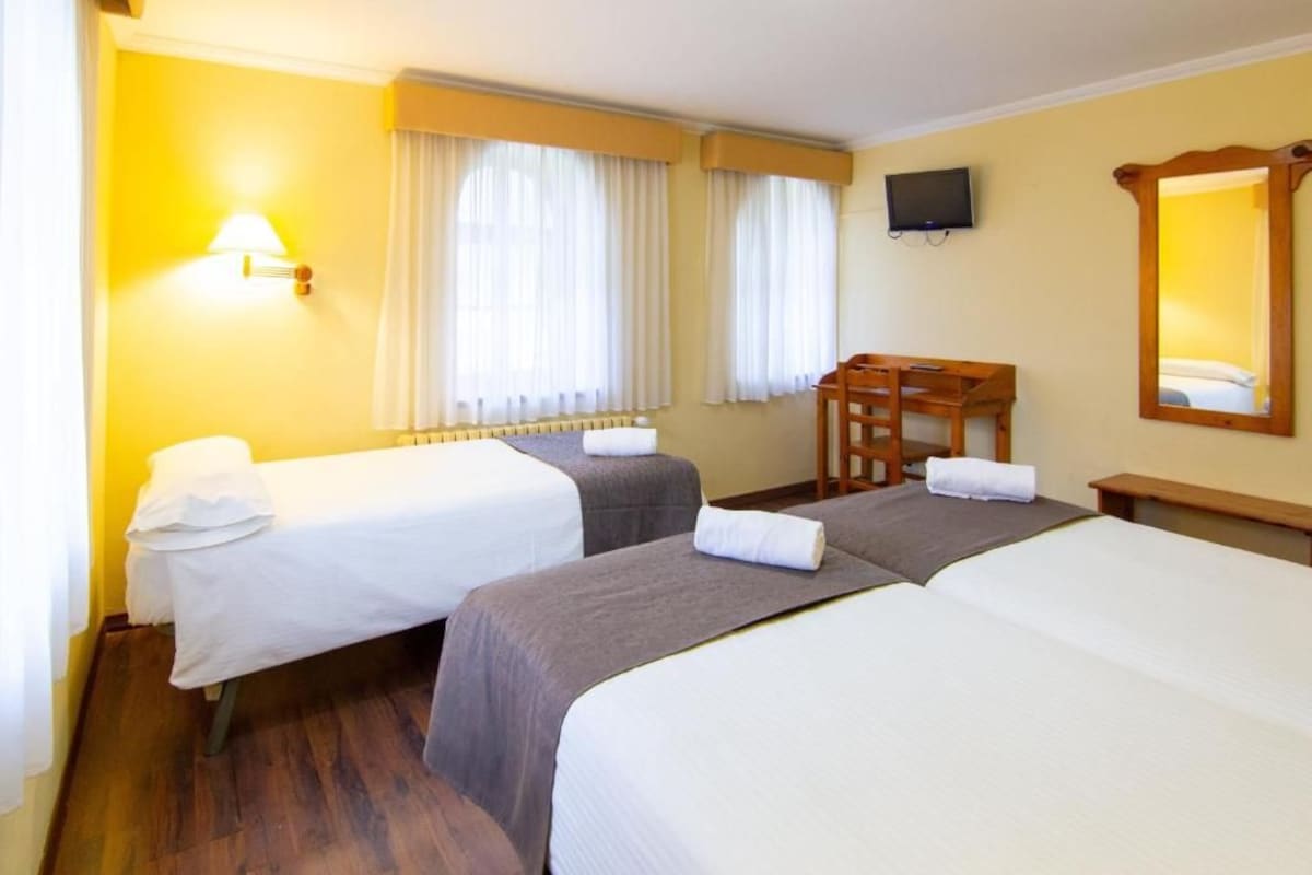 A hotel room with two beds, a desk, a chair, a television, and a mirror.