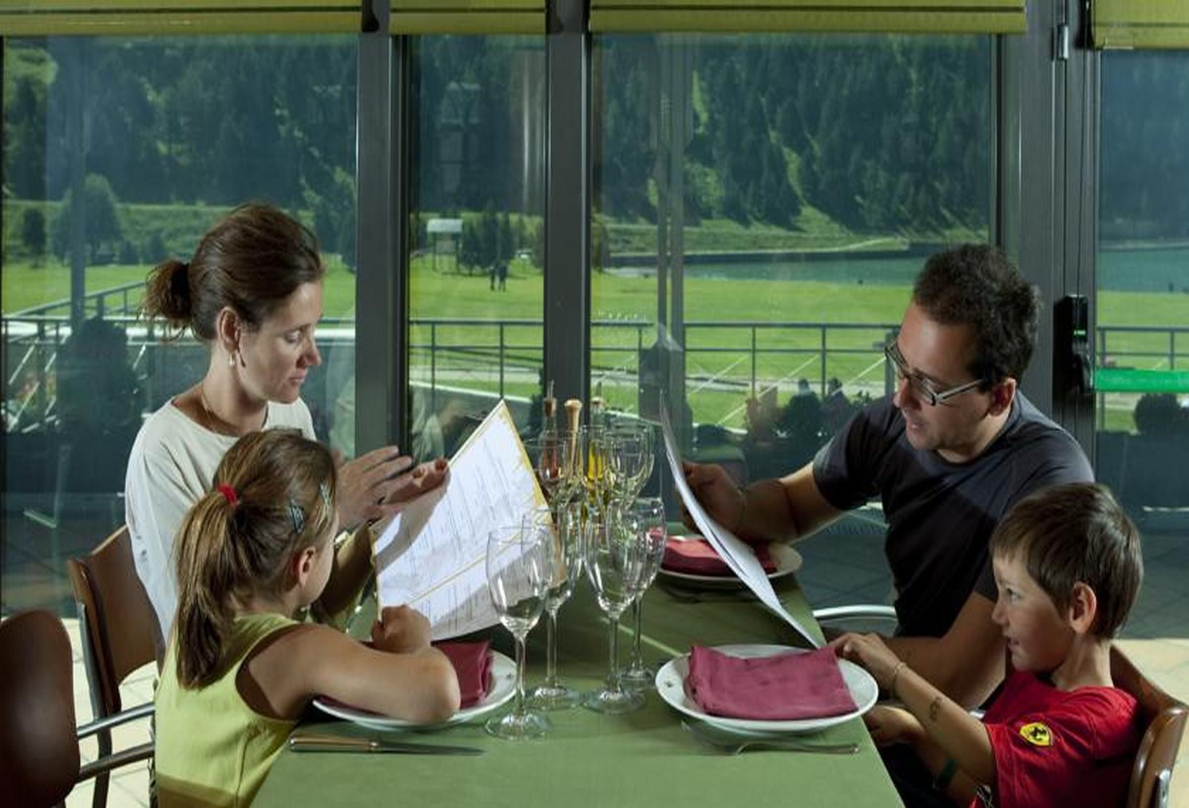 Una familia cenando en una mesa con vistas a un paisaje verde a través de amplias ventanas.