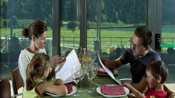 Una familia cenando en una mesa con vistas a un paisaje verde a través de amplias ventanas.