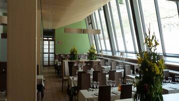 Un restaurante con varias mesas, sillas y amplios ventanales que dejan entrar luz natural.