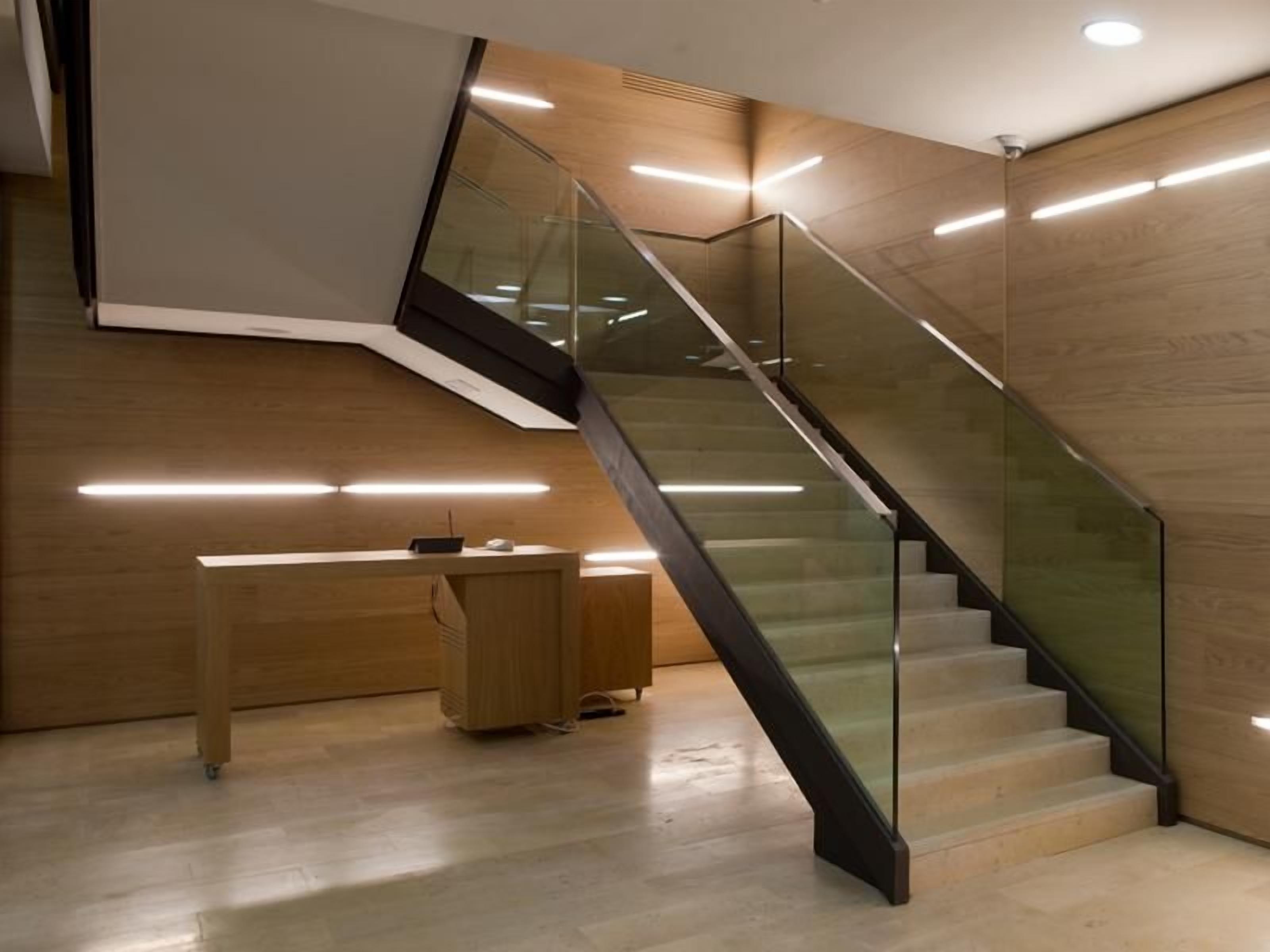 Un interior moderno con una escalera de cristal, suelo de madera y un escritorio con una computadora.