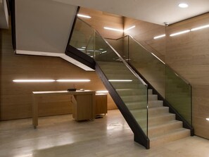 A modern interior with a glass staircase, wooden flooring, and a desk with a computer.