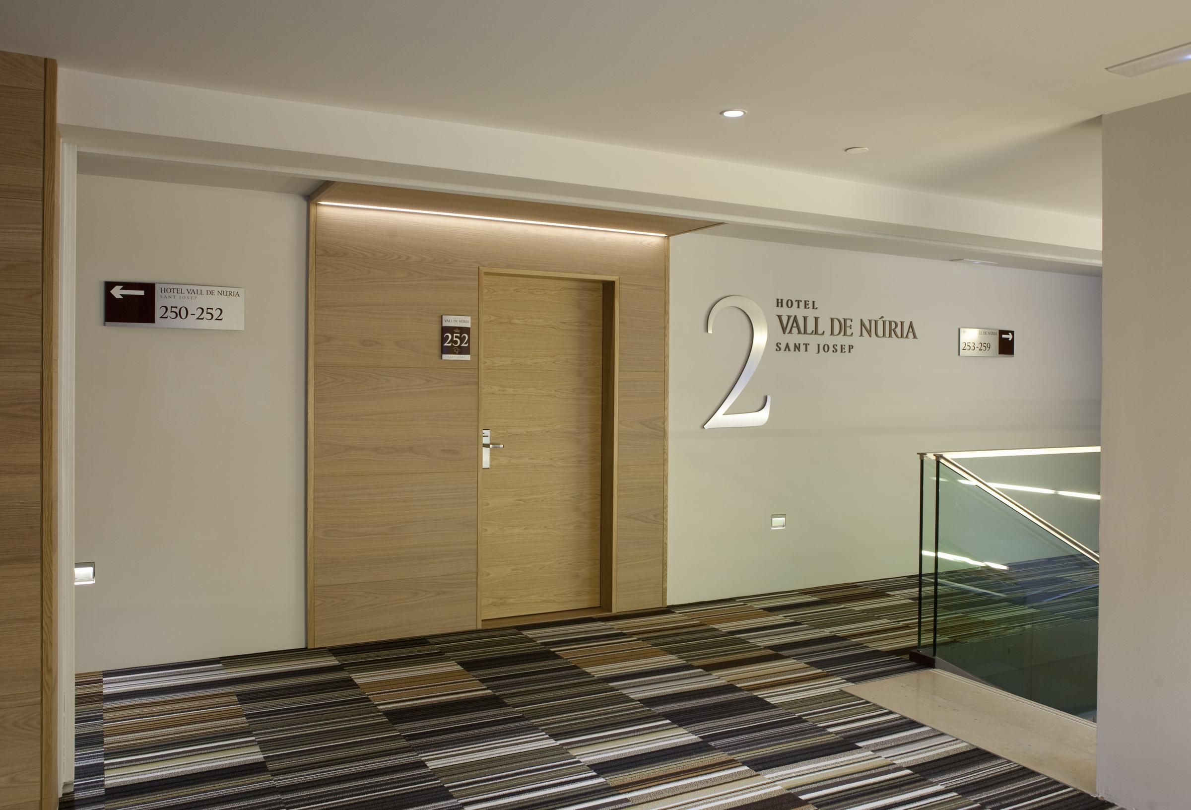 Interior de hotel con diseño moderno, que incluye una puerta de madera, un cartel con número y una escalera con alfombra estampada.