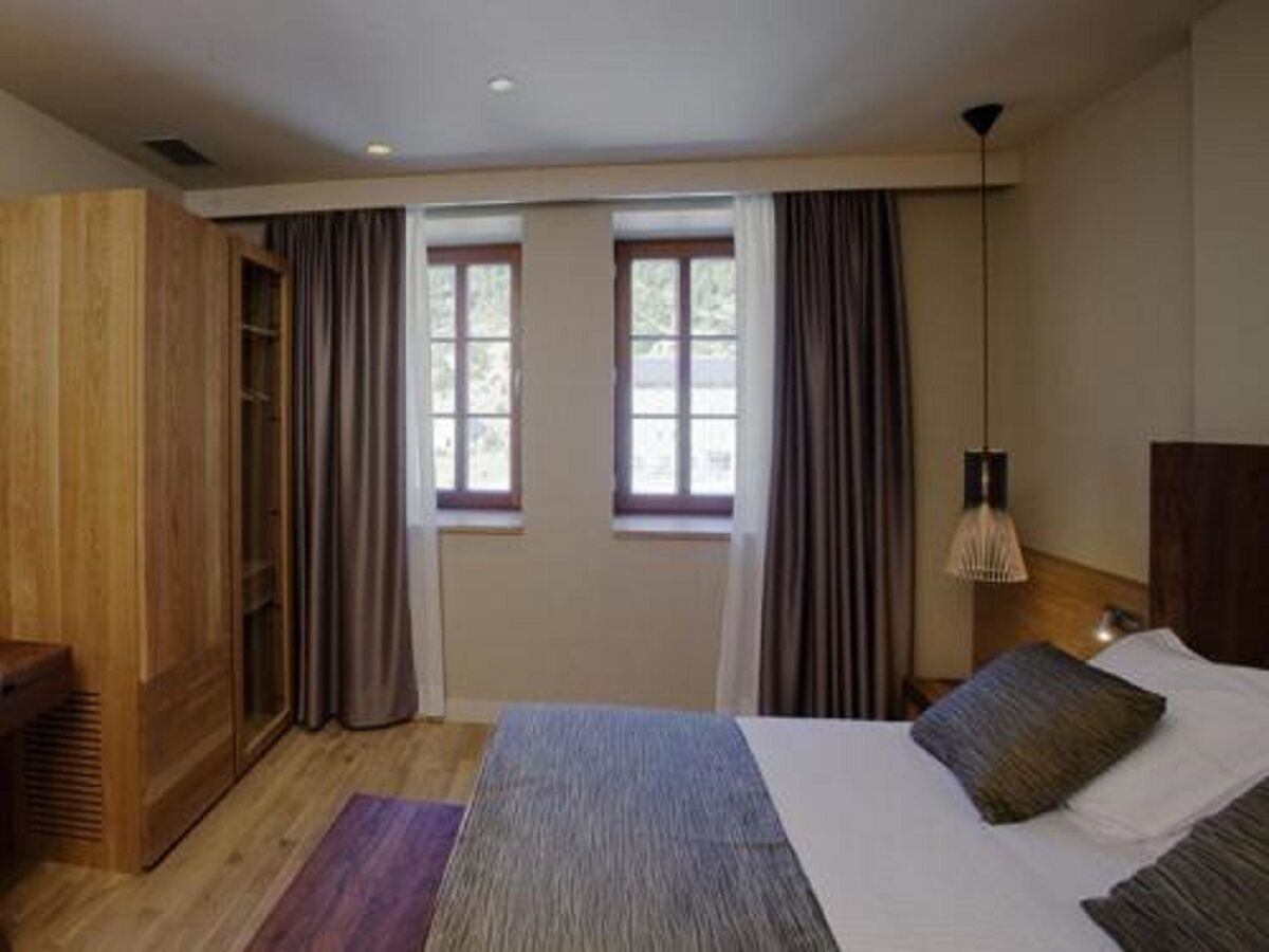 Un dormitorio con una cama, un armario de madera, una ventana con cortinas y una lámpara de noche.
