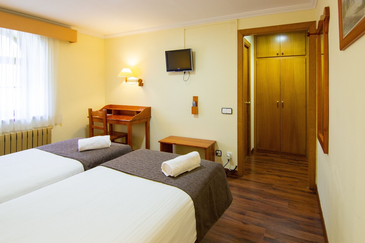 A hotel room with two beds, a desk, a television, and a wardrobe.
