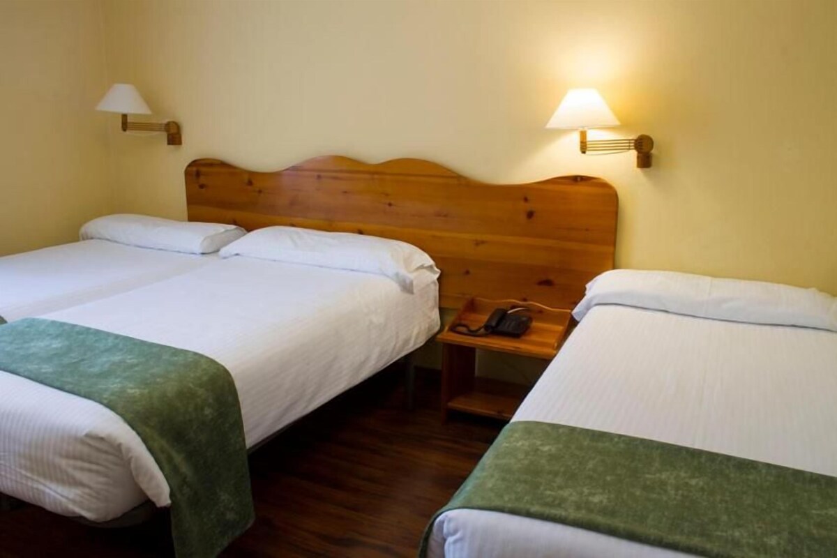 A hotel room with two single beds, wooden headboards, bedside lamps, and a telephone on a nightstand.