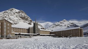 Un bâtiment doté de nombreuses fenêtres et d’une tour centrale, entouré de montagnes enneigées.
