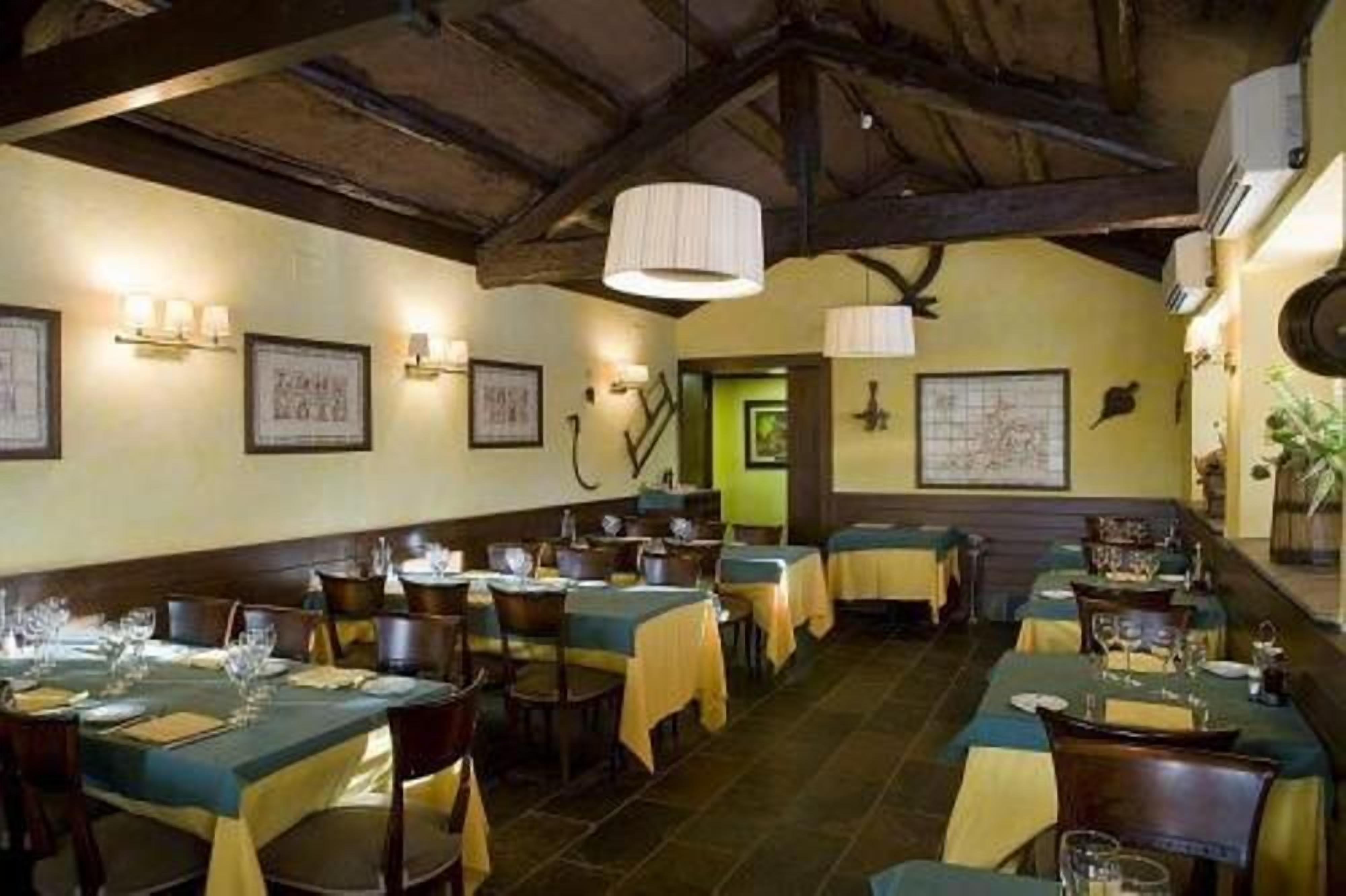 Un restaurante con varias mesas dispuestas para comer, que presenta un interior rústico con vigas de madera a la vista e iluminación instalada en la pared.