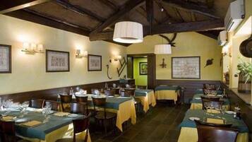 Un restaurante con varias mesas dispuestas para comer, que presenta un interior rústico con vigas de madera a la vista e iluminación instalada en la pared.