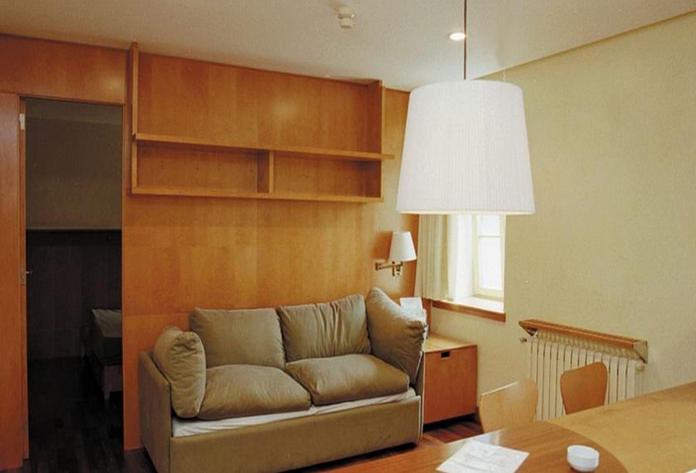 Una habitación con sofá, una mesa, lámpara y ventana.