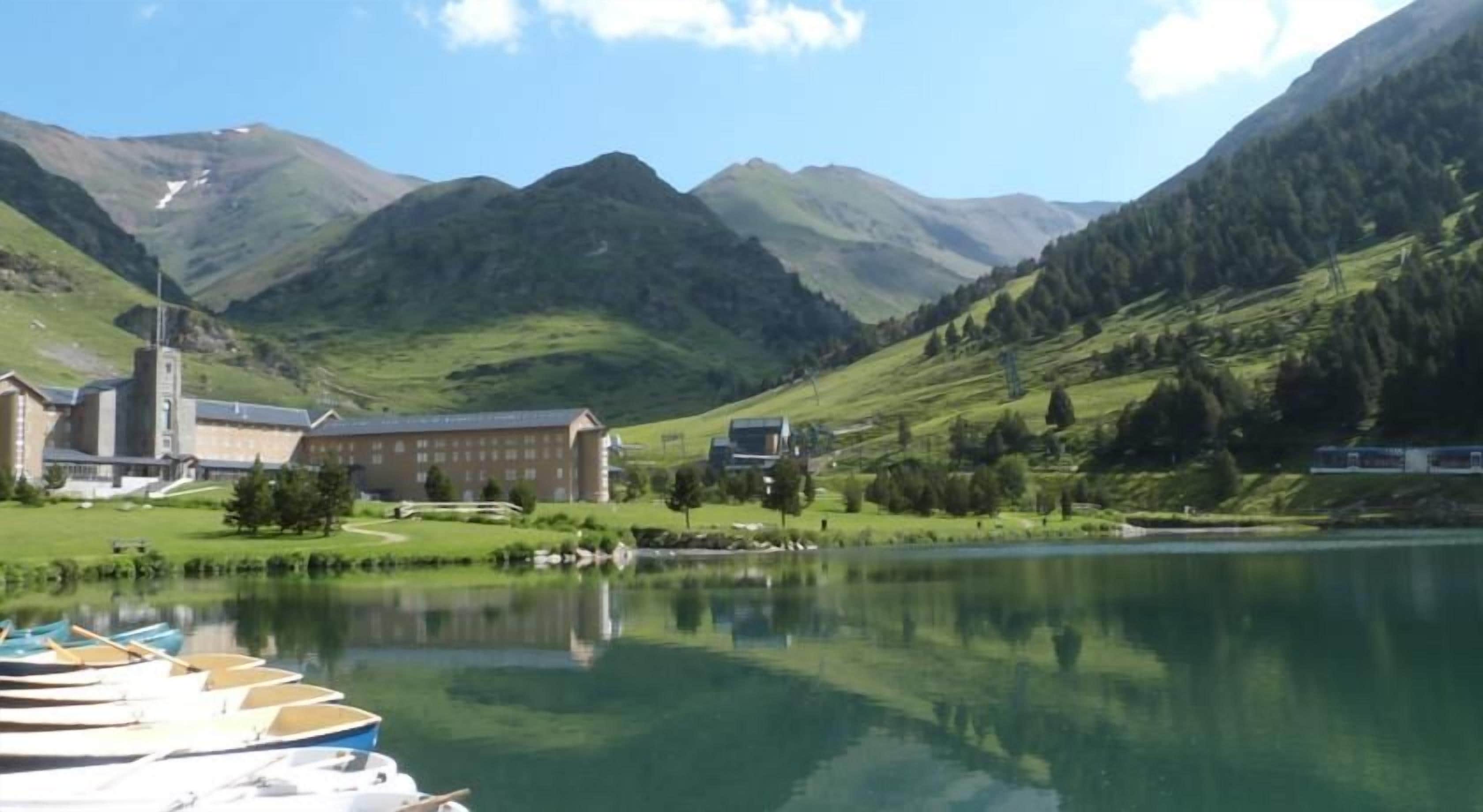 A lake with boats, a building, and mountains in the background.