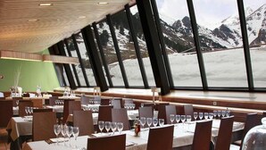A restaurant with tables set for dining, large windows with a view of snow-covered mountains. - Vall de Nuria (Queralbs)