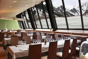 Un restaurante con mesas dispuestas para comer, amplios ventanales que ofrecen vistas a montañas nevadas.