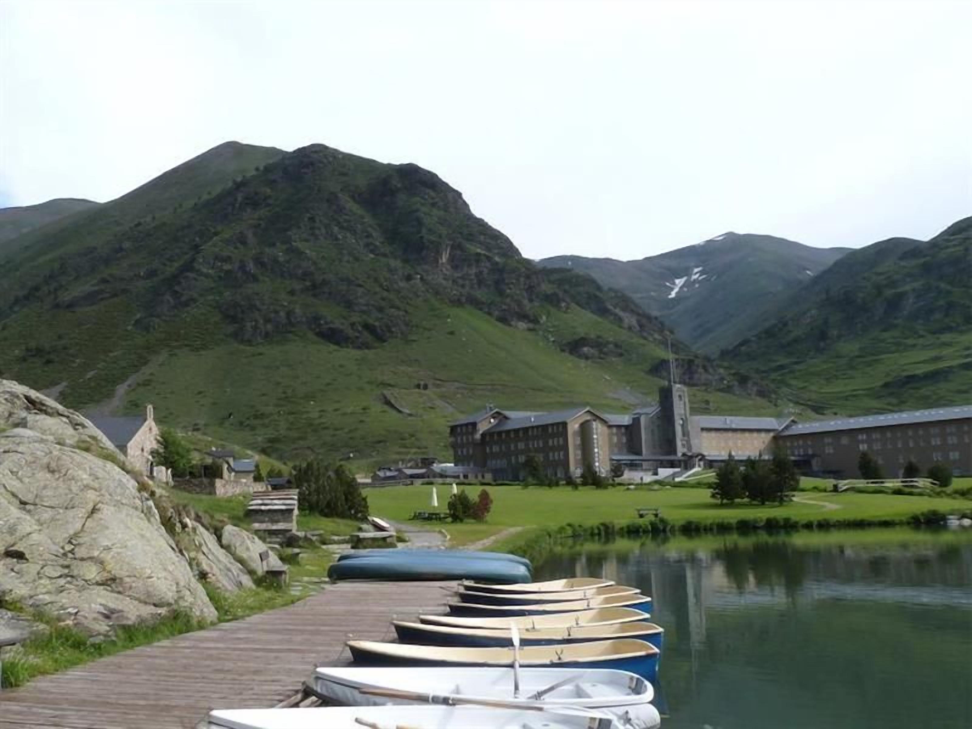Un edificio junto al lago con un muelle y barcos, rodeado de montañas.