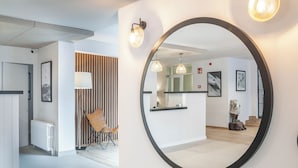 A modern hotel lobby with a large mirror, a reception desk, a wooden slat wall, and a seating area. - Hotel Viella (Vielha e Mijaran)