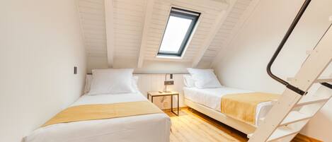 A small, well-lit room with two beds, a skylight, and a wooden floor.