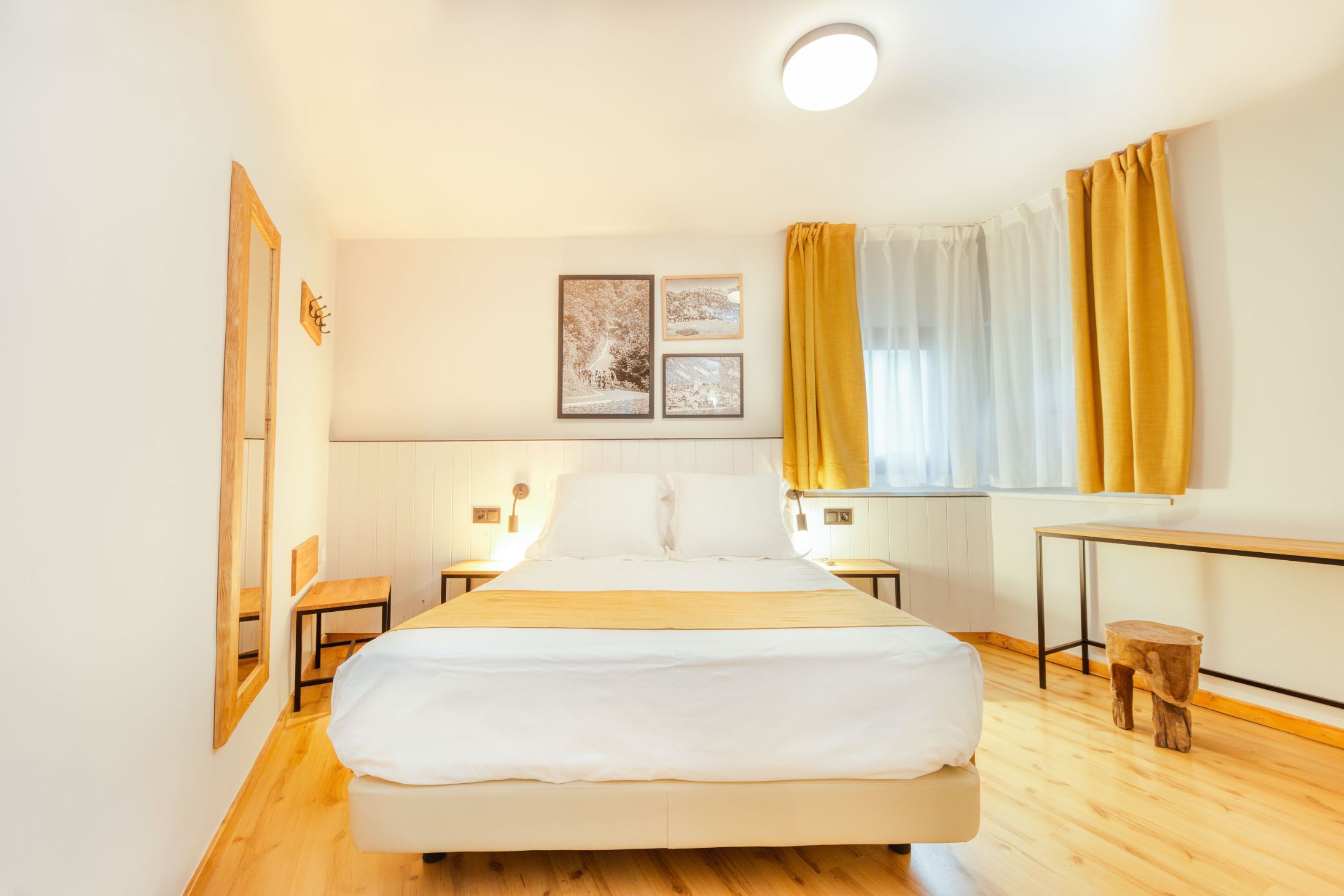 A neatly arranged bedroom with a large bed, bedside tables, a small stool, and a window with curtains.