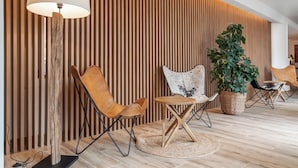 A modern interior with a wooden slatted wall, a floor lamp, leather chairs, a small table, and a potted plant. - Hotel Viella (Vielha e Mijaran)