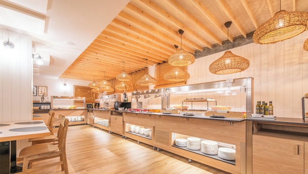 A modern kitchen with wooden flooring, a central island with a sink, and overhead wicker pendant lighting. - Hotel Viella (Vielha e Mijaran)