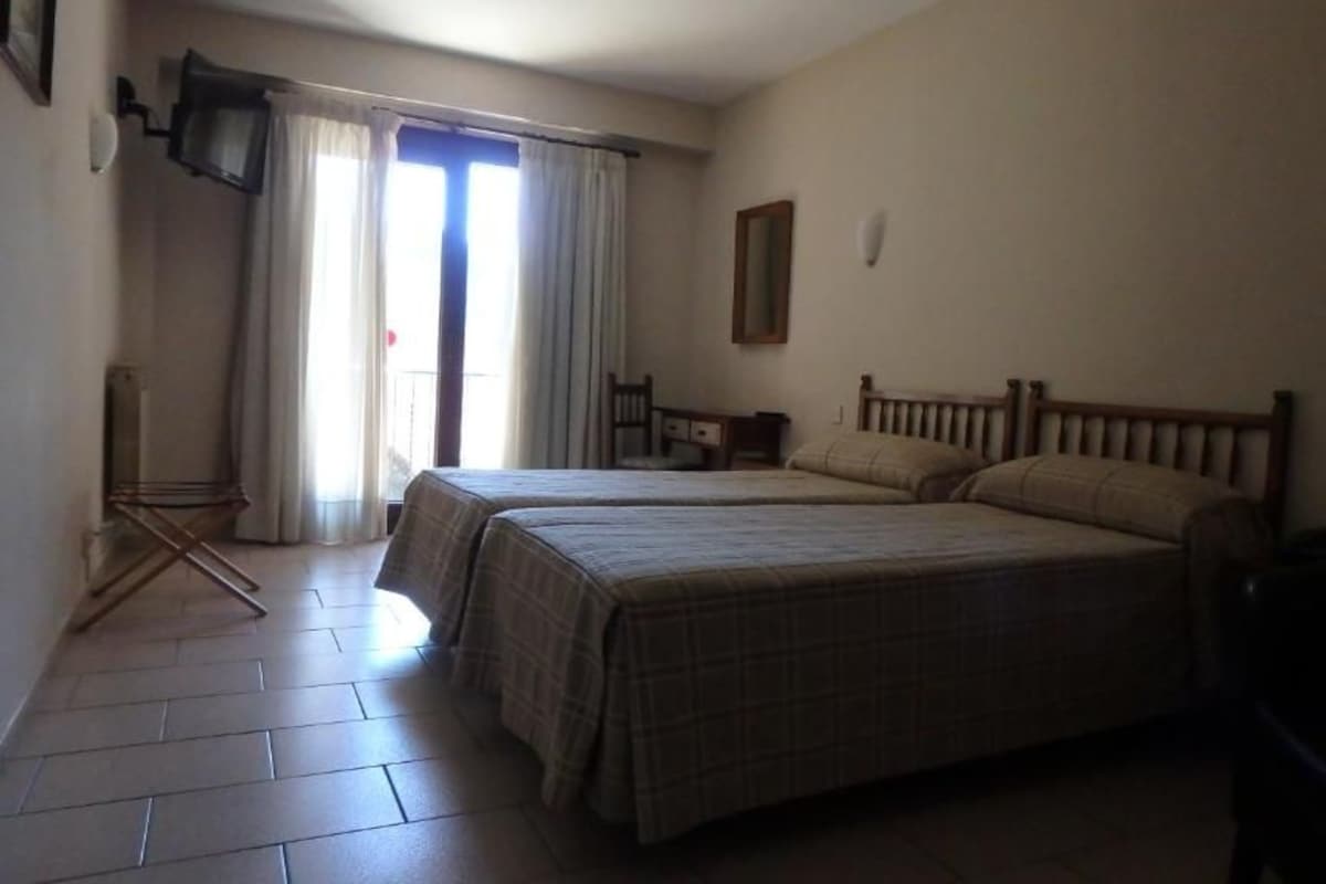 Une chambre avec deux lits, une chaise, une petite table et un téléviseur.