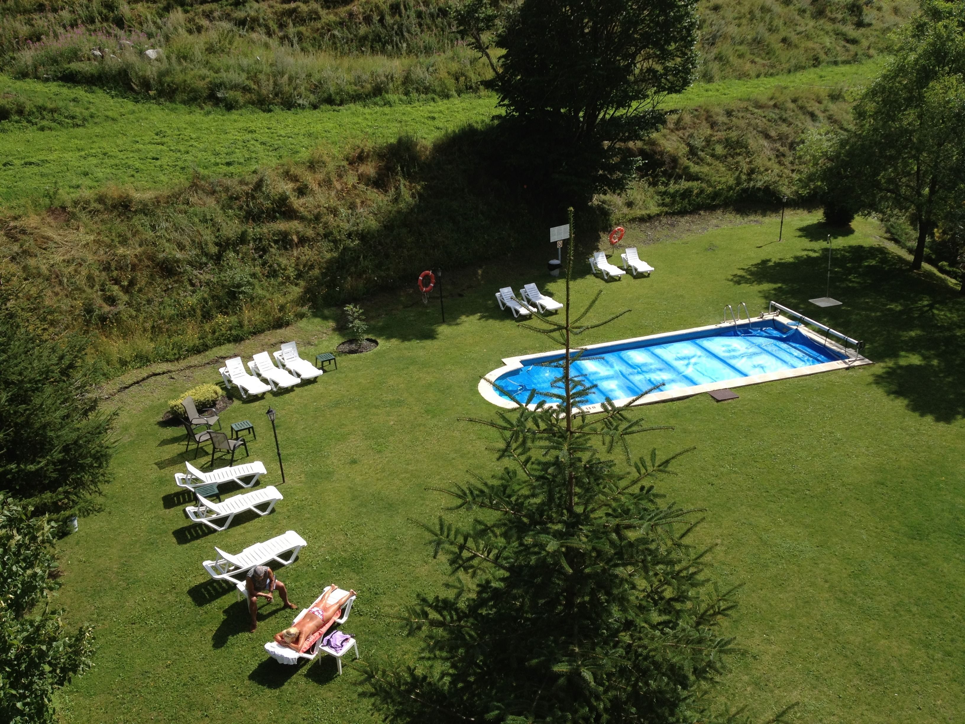 An aerial view of a swimming pool surrounded by lawn chairs and sun loungers, with a grassy area and trees in the background.