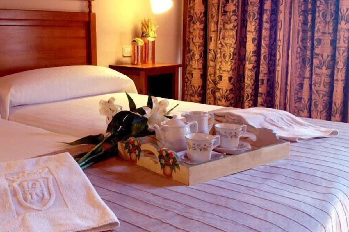 A neatly made bed with white linens, a tray with tea set, and a towel with a crest.