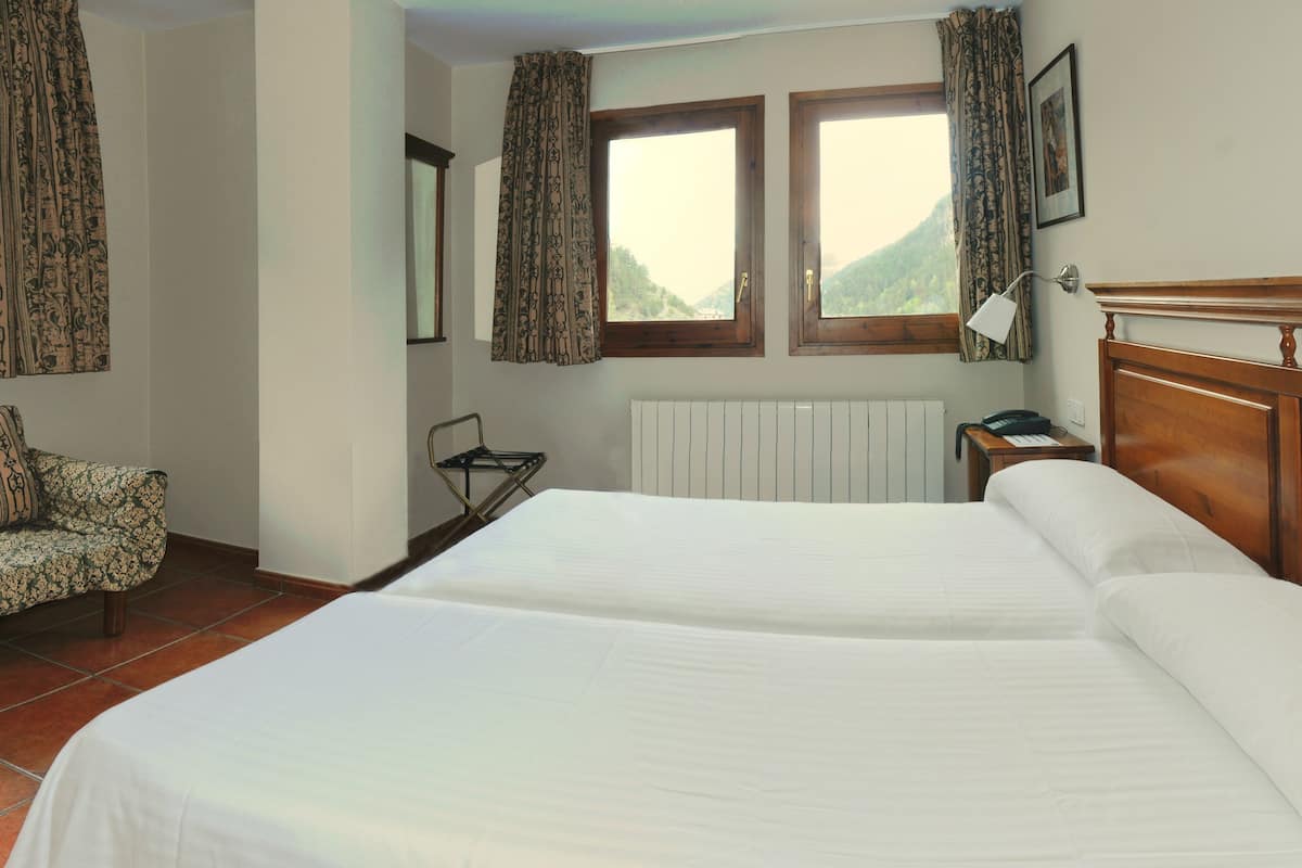 A bedroom with a bed, a sofa, two windows with curtains, a radiator, and a lamp.