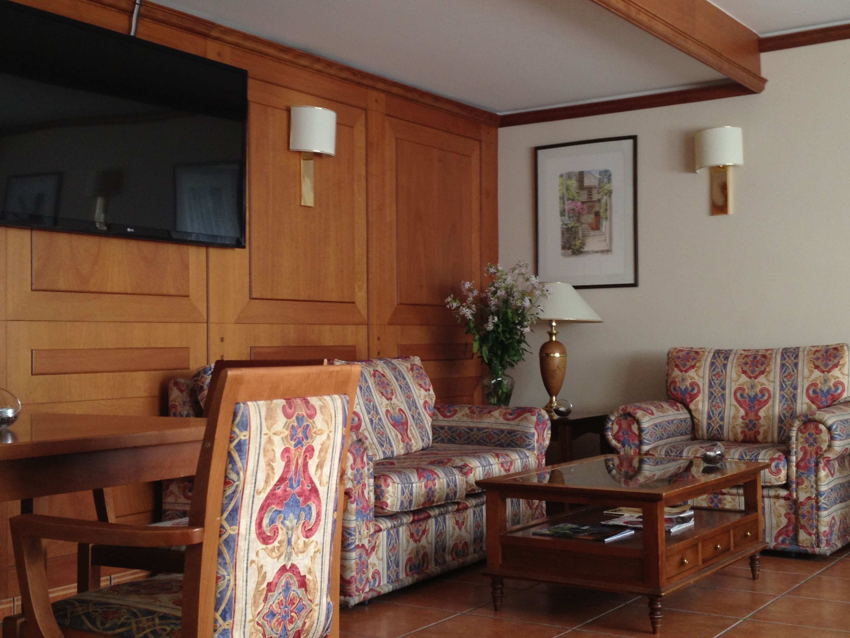 Una sala de estar con un mueble bajo de televisión de madera, sofás estampados, una mesa de centro y dos lámparas fijadas a la pared.