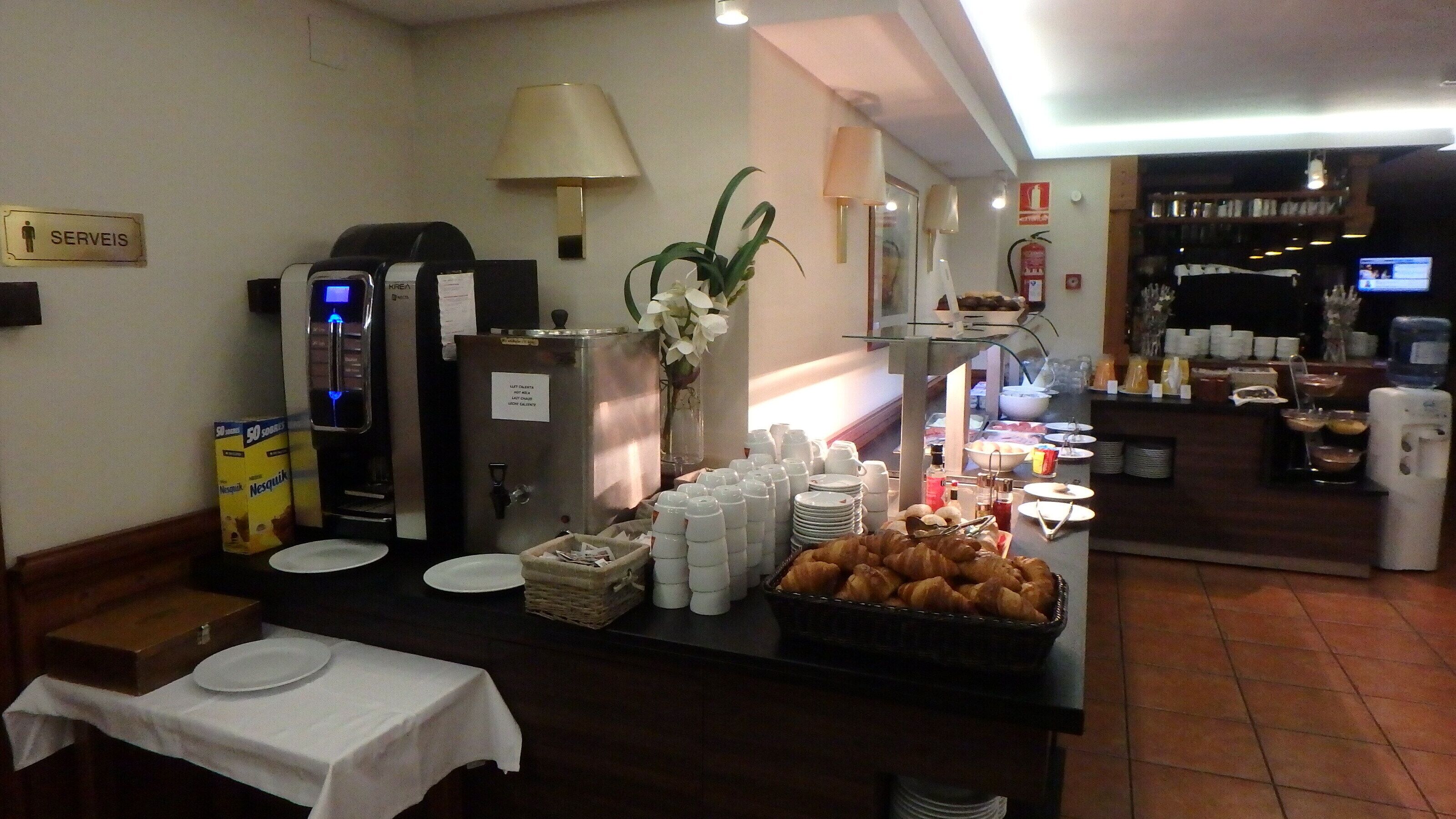 A breakfast buffet setup with coffee machines, plates, and a variety of food items.