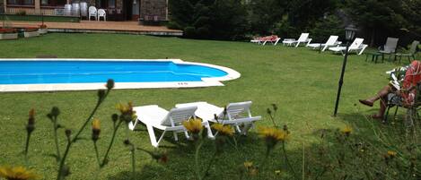 Zona de piscina con sillones de descanso y un edificio al fondo.
