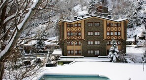 A multi-story hotel with a stone facade, large windows, and a snow-covered landscape. - Hotel Xalet Verdú (Arinsal)