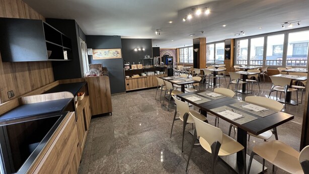 Un restaurant moderne dont le décor combine des éléments en bois et en métal, avec un comptoir central et de grandes fenêtres qui laissent entrer la lumière naturelle.