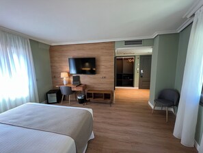 A hotel room with a bed, desk, chair, TV, and a walk-in closet.