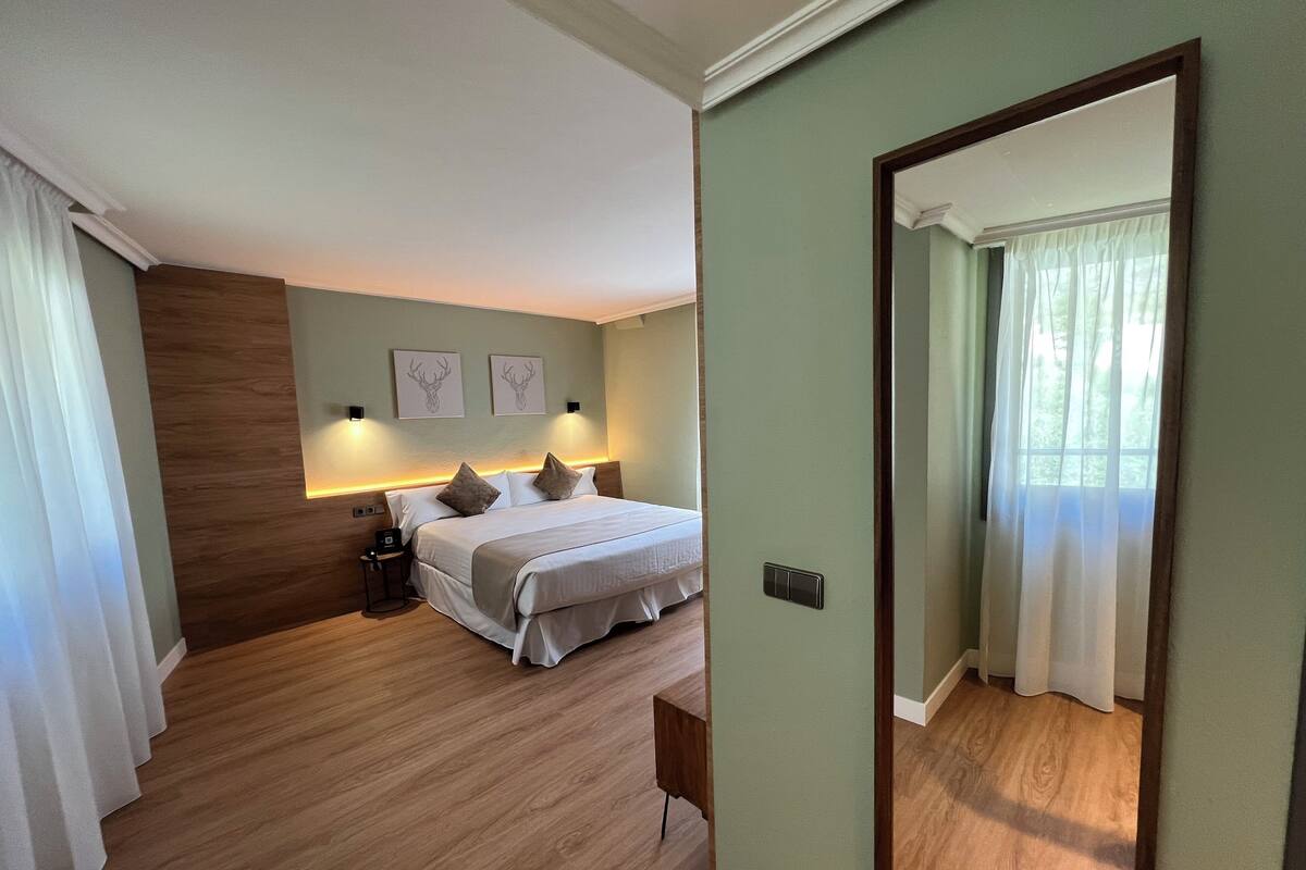 Een hotelkamer met een bed, nachtkastjes, een spiegel en uitzicht op het omliggende landschap.