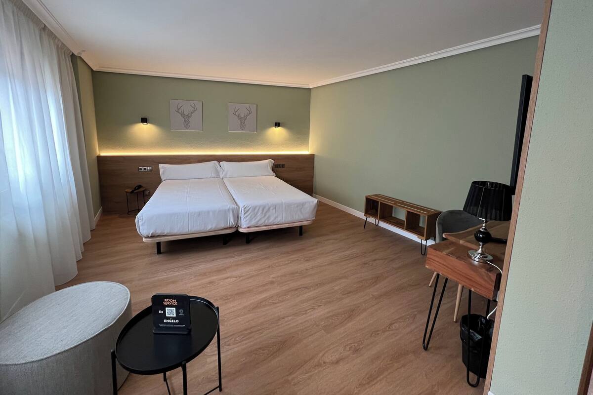 Een hotelkamer met een tweepersoonsbed, nachtkastjes, een bureau met stoel, een klein rond tafeltje en een tv aan de muur.